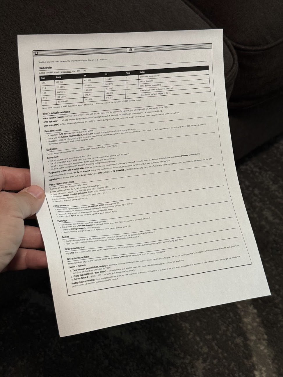 Person holding a printed technical reference sheet with frequency table and specifications for amateur radio operations